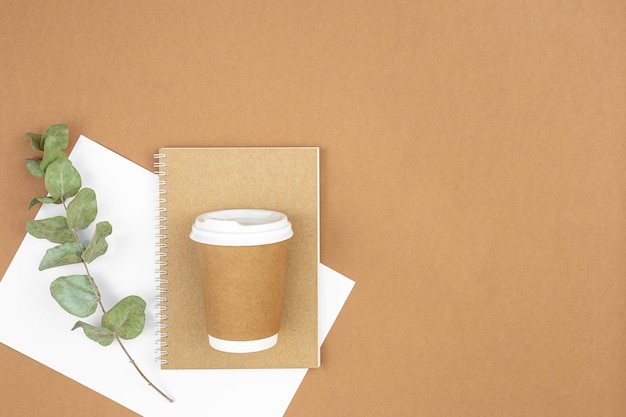 Craft paper coffee cup notebook and eucalyptus sprig on eco background flat lay