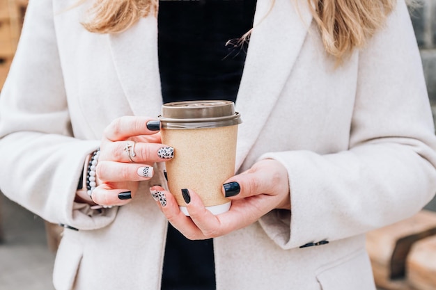 Craft paper coffee cup in woman hands with perfect manicure Drinking take away coffee Nail autumn concept