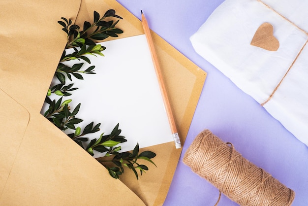빈 종이와 녹색 잔가지가 있는 공예 종이 봉투와 묶음 와인딩 및 선물을 매우 가까운 뒷면에 에코 패키지로 제공