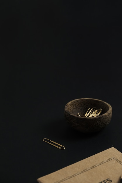 Craft paper notebook, pencil, clips in wooden bowl on black