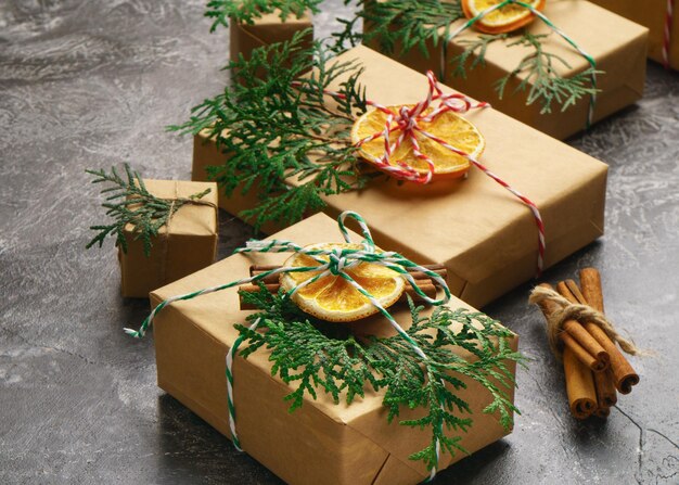 Craft Paper Presents Boxes Cord Fir Tree Branch Dry Sliced Orange Fruit Cinnamon Sticks on Concrete Background. Christmas Gift Concept Top View. New Year Preparation Background.