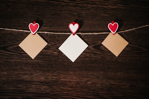 Craft paper, three blank, with red heart hanging on lacing or rope on brown wooden wall with space. Place for text. concept of St. Valentine's Day.