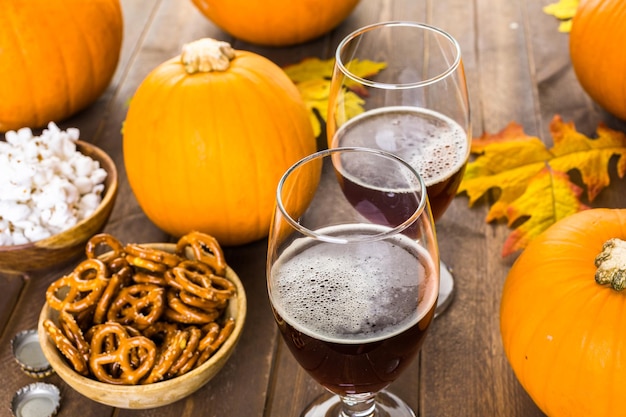 Craft pumpkin beer in beer glasses with salty pretzels and popcorn.