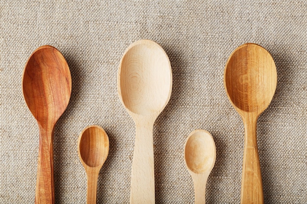 Craft spoons made from different types of wood lie in a row on a hemp burlap fabric