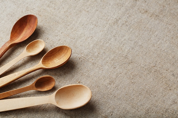 Craft spoons made from different types of wood lie in a row on a hemp burlap fabric