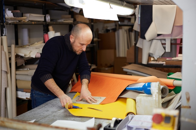 Craftsman cutting leather with cutter in workshop