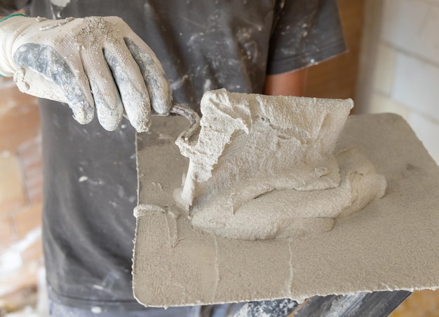 craftsman in dirty gloves puts plaster mortar or cement on a metal trowel men in a gray shirt