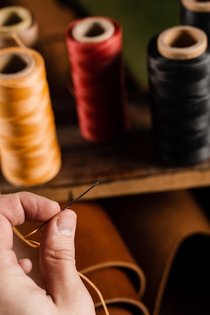 Craftsman is holding needle with thread on roll of brown genuine leather background in craftsman workshop Handmade genuine leather production in the factory