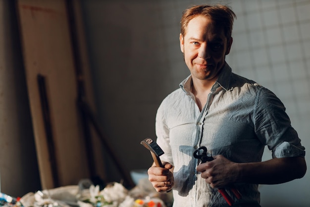 Foto il ritratto del maestro maschio dell'artigiano tiene in mano il martello e i pezzi di vetro smalt per le opere d'arte del mosaico in officina