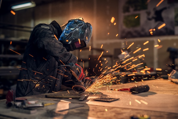 Photo craftsman sawing metal, sparkles around workshop