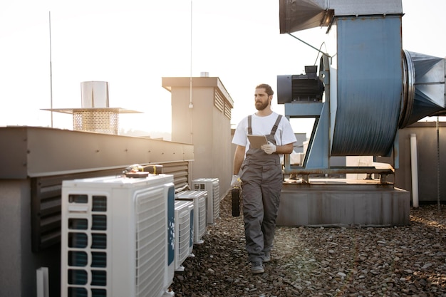 Photo craftsman walking by conditioners and holding tablet on roof