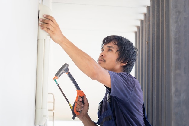 Photo craftsman worker sawing a pipe technician man installing an air conditioning in a client house young repairman fixing air conditioner unit maintenance and repairing concepts