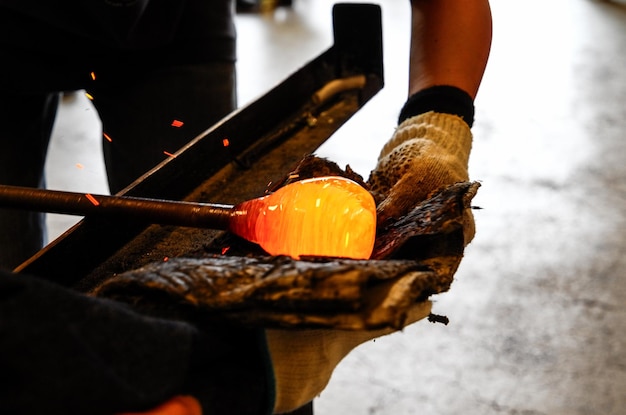 craftsperson holding blowpipe with molten glass at workshop