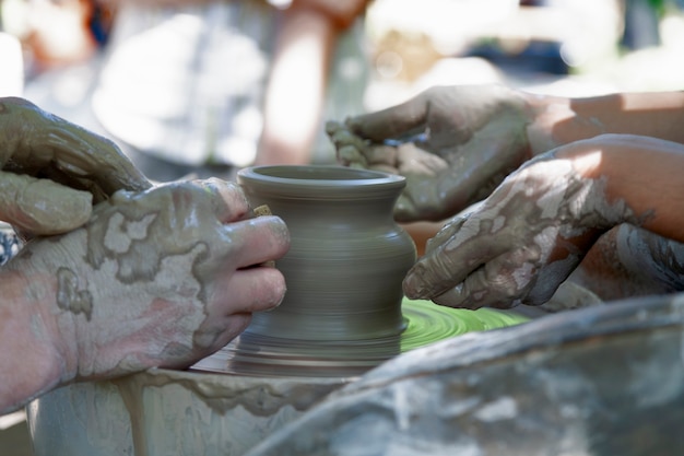 Foto le mani di un'artigiana che guidano un'altra mano, per insegnargli a lavorare con la ruota in ceramica.