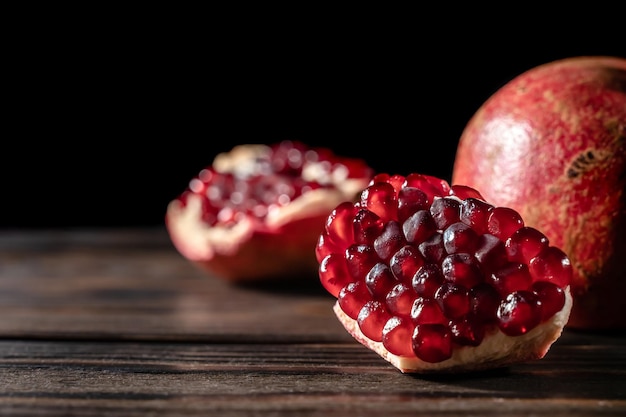 Photo craked ripe and one whole pomegranate on dark wooden desk