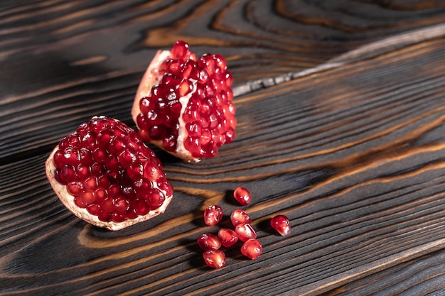 Photo craked ripe pomegranate and garnet seeds on dark wooden desk with place for text, top view