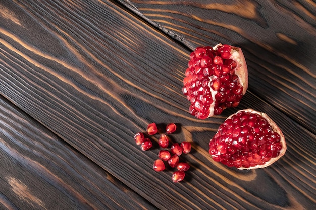 Craked ripe pomegranate and garnet seeds on dark wooden desk with place for text, top view