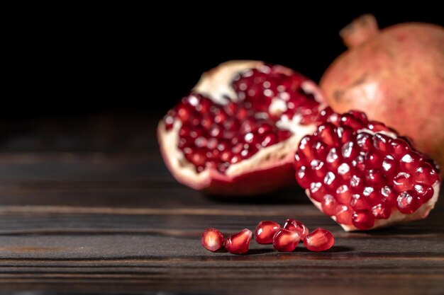 Craked ripe pomegranate and garnet seeds on dark wooden desk with place for text