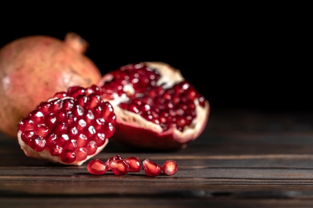 Craked ripe pomegranate and garnet seeds on dark wooden desk with place for text