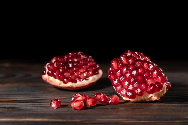 Photo craked ripe pomegranate and garnet seeds on dark wooden desk with place for text