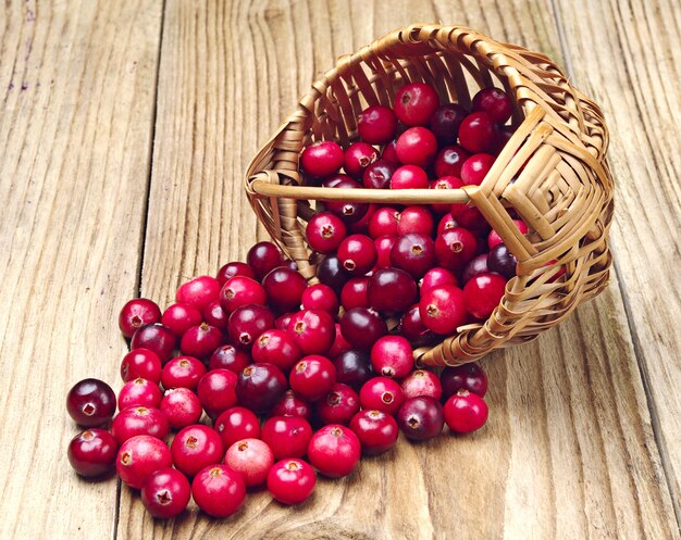 Cranberries near the basket on wooden background