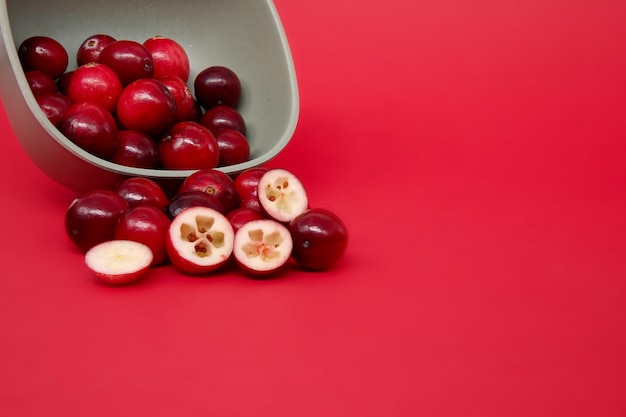 Cranberries spilled out of the bowl scattering on the surface with halfcut cranberry in front