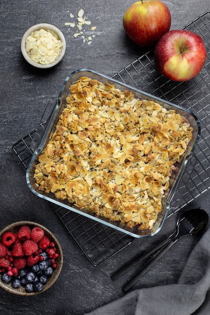 Cranberry and apple crumble, crisp in a glass baking dish with almond flakes and fresh berries on dark stone concrete.