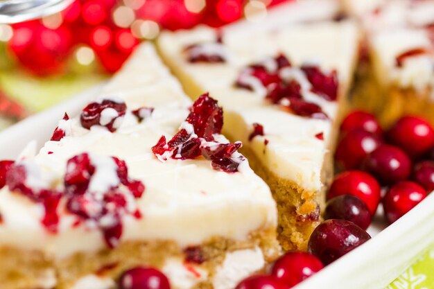 Cranberry bliss bar made with chunks of white chocolate and dried cranberries, topped with sweet cream cheese icing.