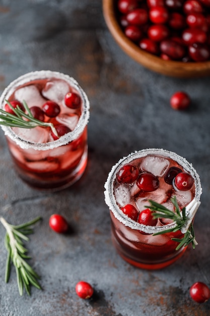 Cocktail di mirtilli rossi con ghiaccio. bevanda di mirtillo rosso di natale in bicchieri decorati con zucchero e rosmarino