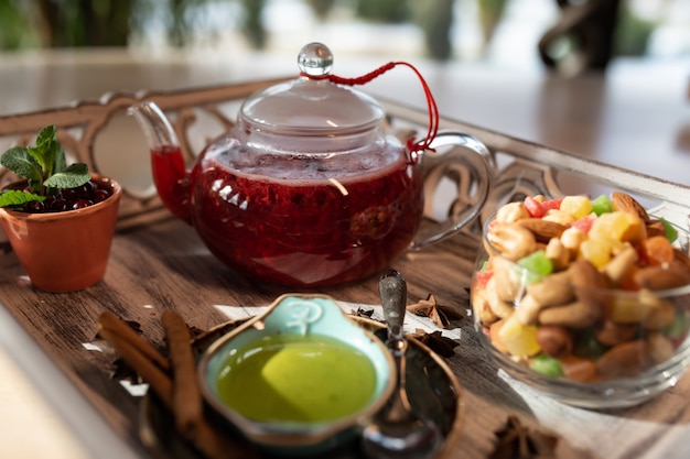 Cranberry ginger tea in a transparent teapot with a plate of nuts on a wooden background