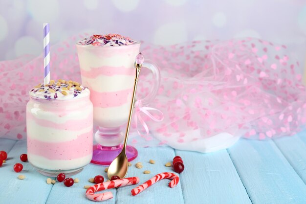 Cranberry milk dessert in glass and glass jar, on color wooden table, on light background