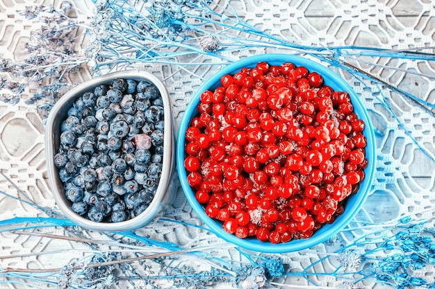 Cranberry in turquoise cup and blueberries in gray bowl on an openwork tablecloth selective focus