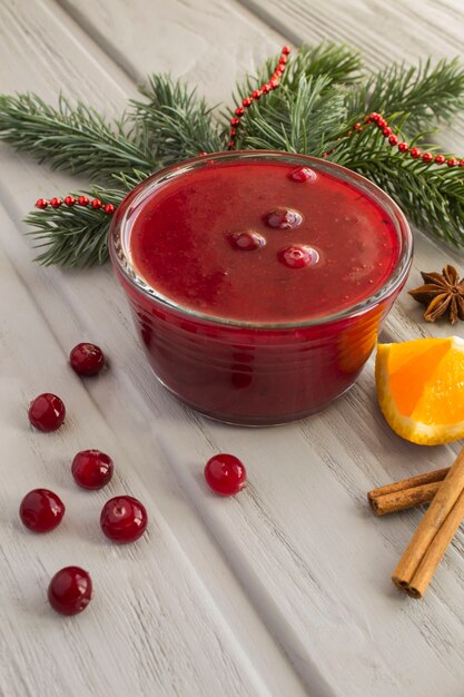 Cranberrysaus in de glazen kom en kerstmissamenstelling op de grijze houten achtergrond. locatie verticaal.