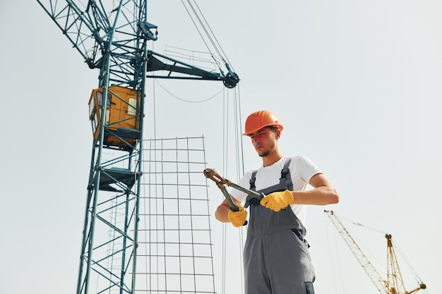 Crane is at background Young construction worker in uniform is busy at the unfinished building