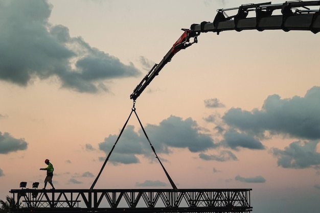 crane loading metal bar with man working at sunset