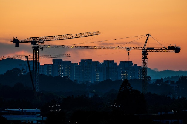 Cranes against buildings during sunset