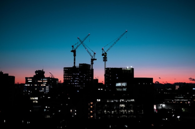 Photo cranes in city against sky at dusk