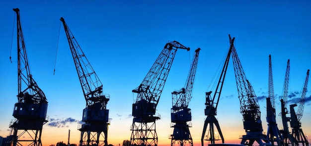 Cranes at commercial dock against clear blue sky