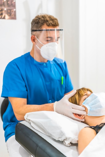 Cranial massage on the head of a physiotherapist with protective measures to a young blonde patient. Covid-19 pandemic. Osteopathy, therapeutic chiromassage