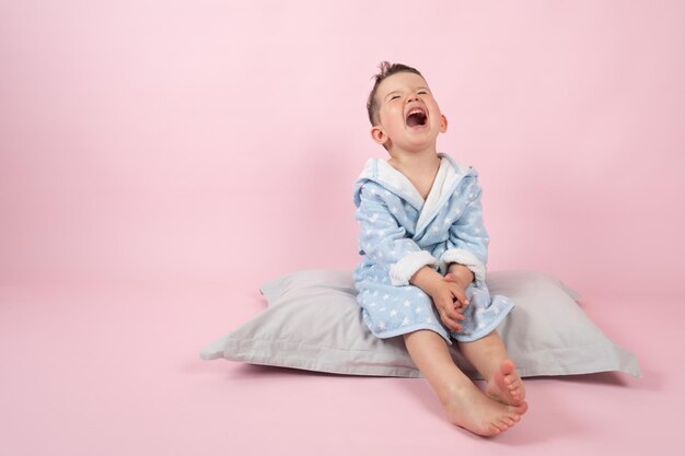 Cranky child boy refuses to go to bed kid boy in bathrobe on\
pink background high quality photo