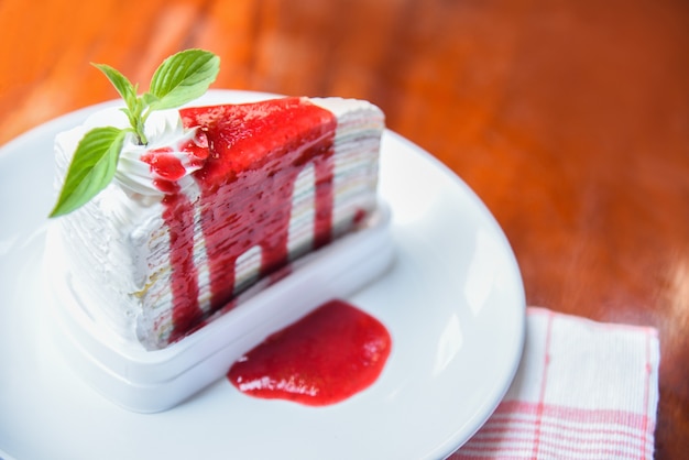 Foto fetta di torta di crape con salsa di fragole sul piatto bianco sul tavolo / arcobaleni piece of cake