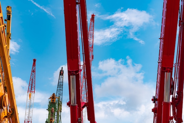 Crawler crane against blue sky and white clouds. Real estate industry. Red crawler crane use reel lift up equipment in construction site. Crane for rent. Crane dealership for construction business.