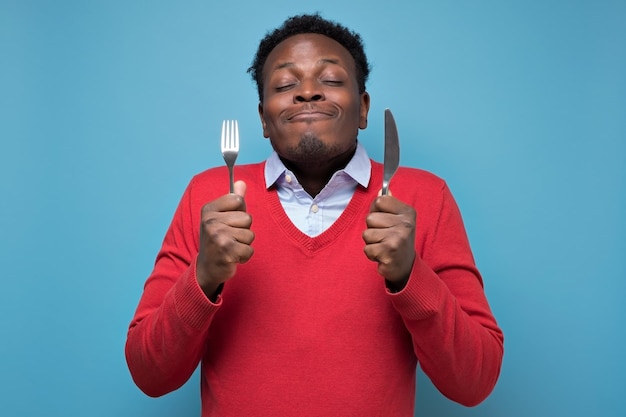 Crazy african american man in red sweater holding a fork and a knife