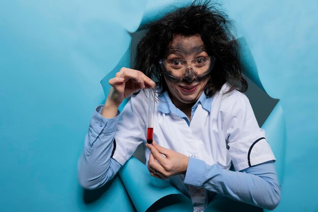 Crazy chemist with wacky goofy look grinning dreadful while presenting glass flask filled with liquid experimental serum. Mad scientist with goofy expression and messy look having glass test tube.