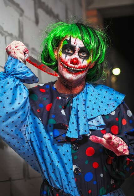 Crazy clown with a knife on a brick wall background. Halloween concept