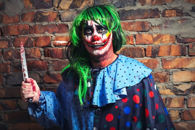 Crazy clown with a knife on a brick wall background. Halloween concept