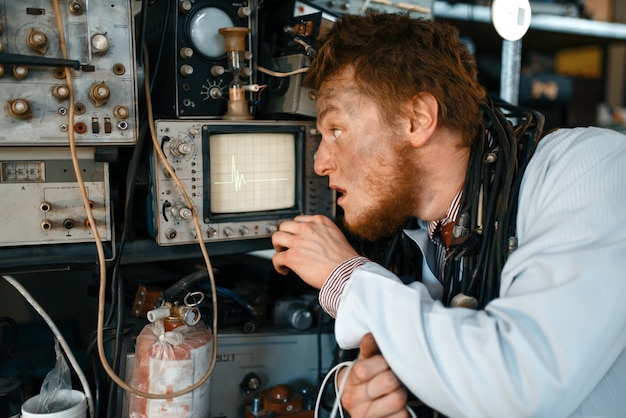 Crazy engineer looks on oscilloscope display in laboratory.