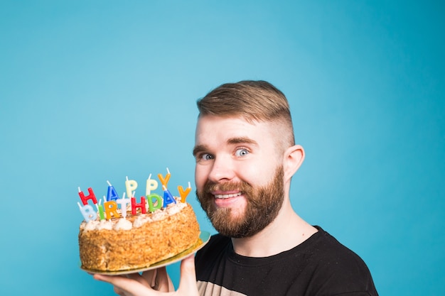 Crazy funny positive guy hipster holding a happy birthday cake in his hands standing on a blue surface