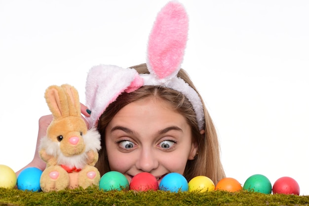 Crazy little girl wearing bunny ears and looking at colorful painted easter eggs. Traditional easter holidays decorations. Happy easter holidays concept.