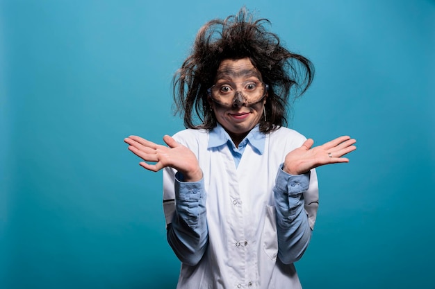 Crazy mad looking chemist with messy hair and dirty face shrugging shoulders after failed chemical experiment explosion. Goofy looking insane scientist on blue background shrugging shoulders.